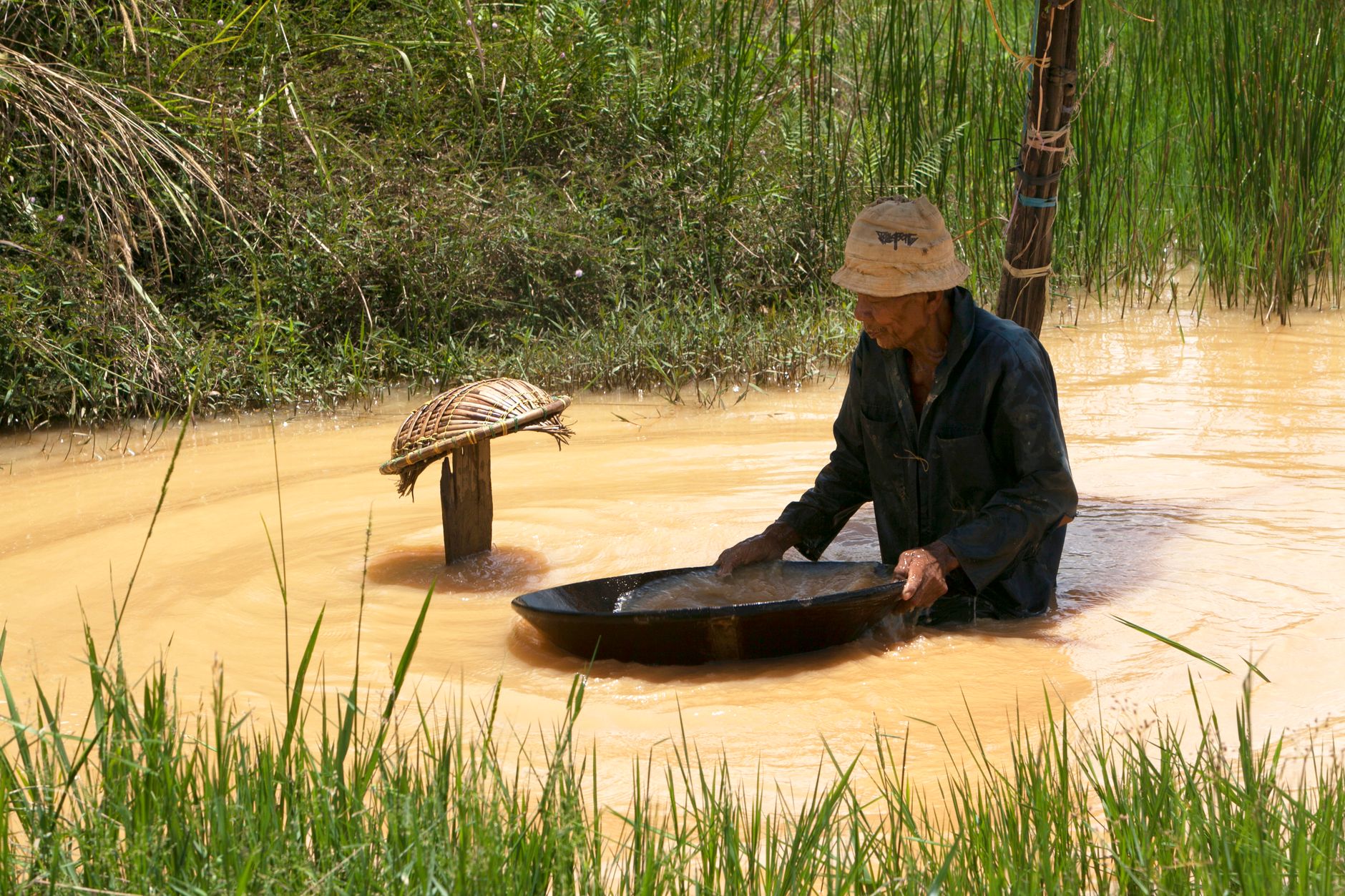 a person's hands working a plastic gold pan underwater in a creek