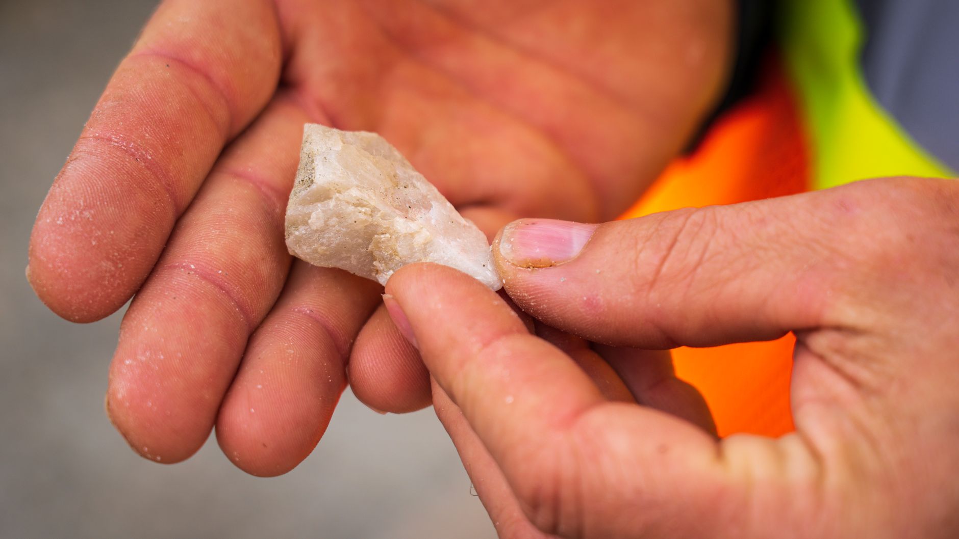 a rockhound examines a mineral specimen with a hand lens in the field