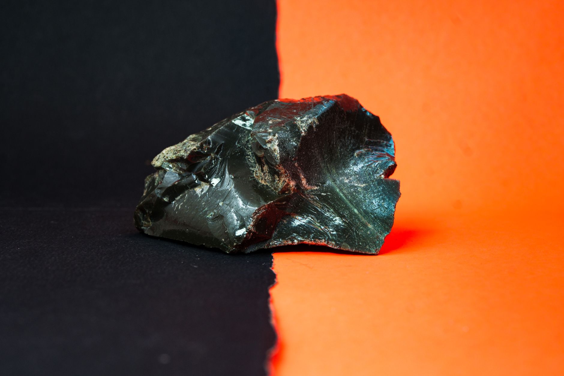 A rough nephrite jade specimen with dark green color and brown rind on rocky ground